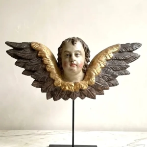A large baroque putti head and stylized wings. Carved wood, painted and partly gilded. Cracking and chips to gesso. South Germany, circa 1750.